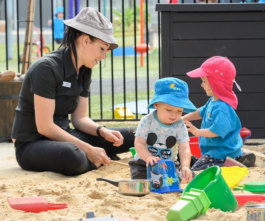 childcare worker playing in sandpit with two children