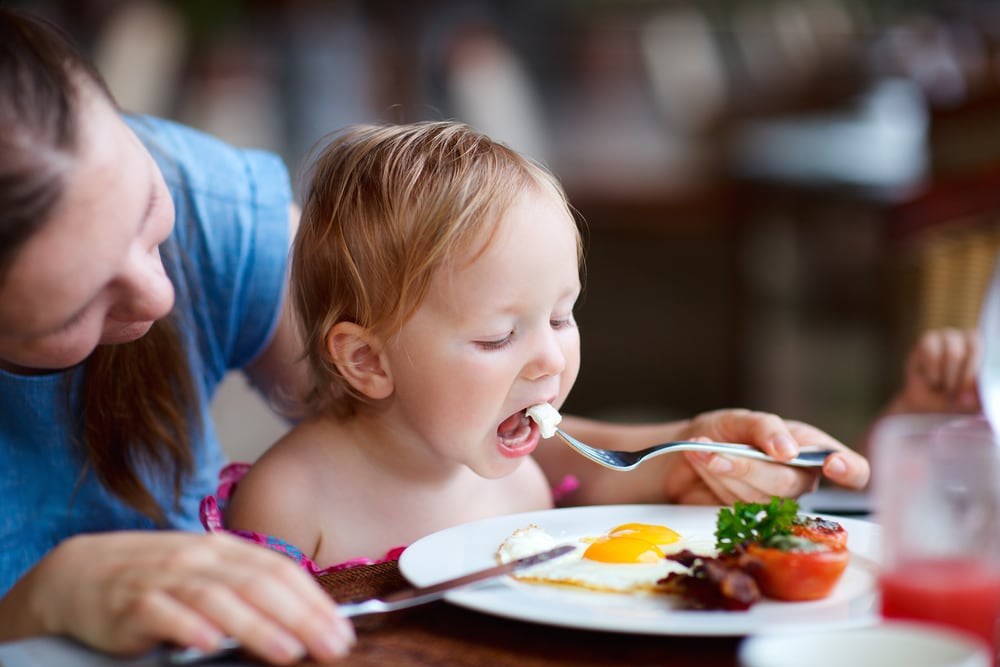 Young mother feeding her daughter some fried eggs for breakfast