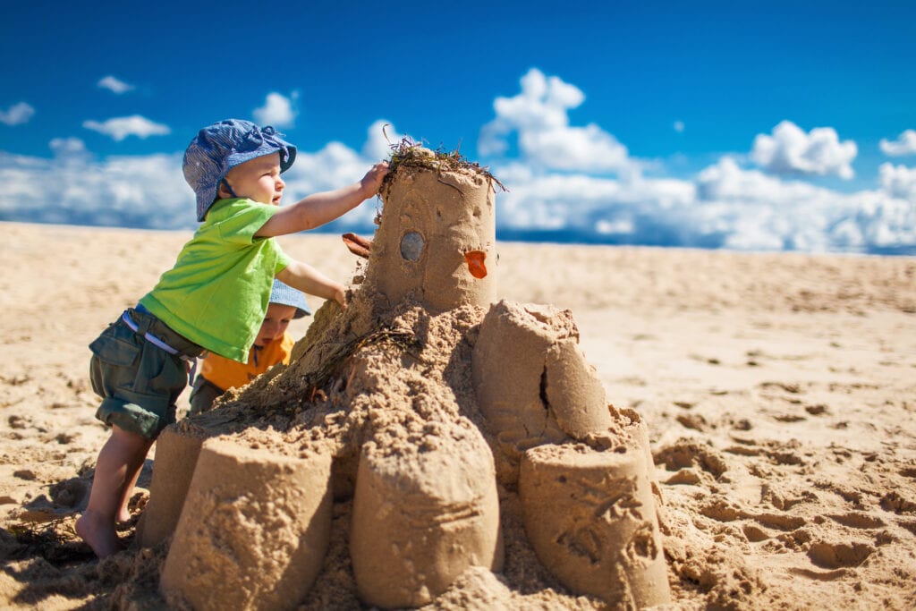 Two little boys in colourful t-shirts building large sandcastle on the beach