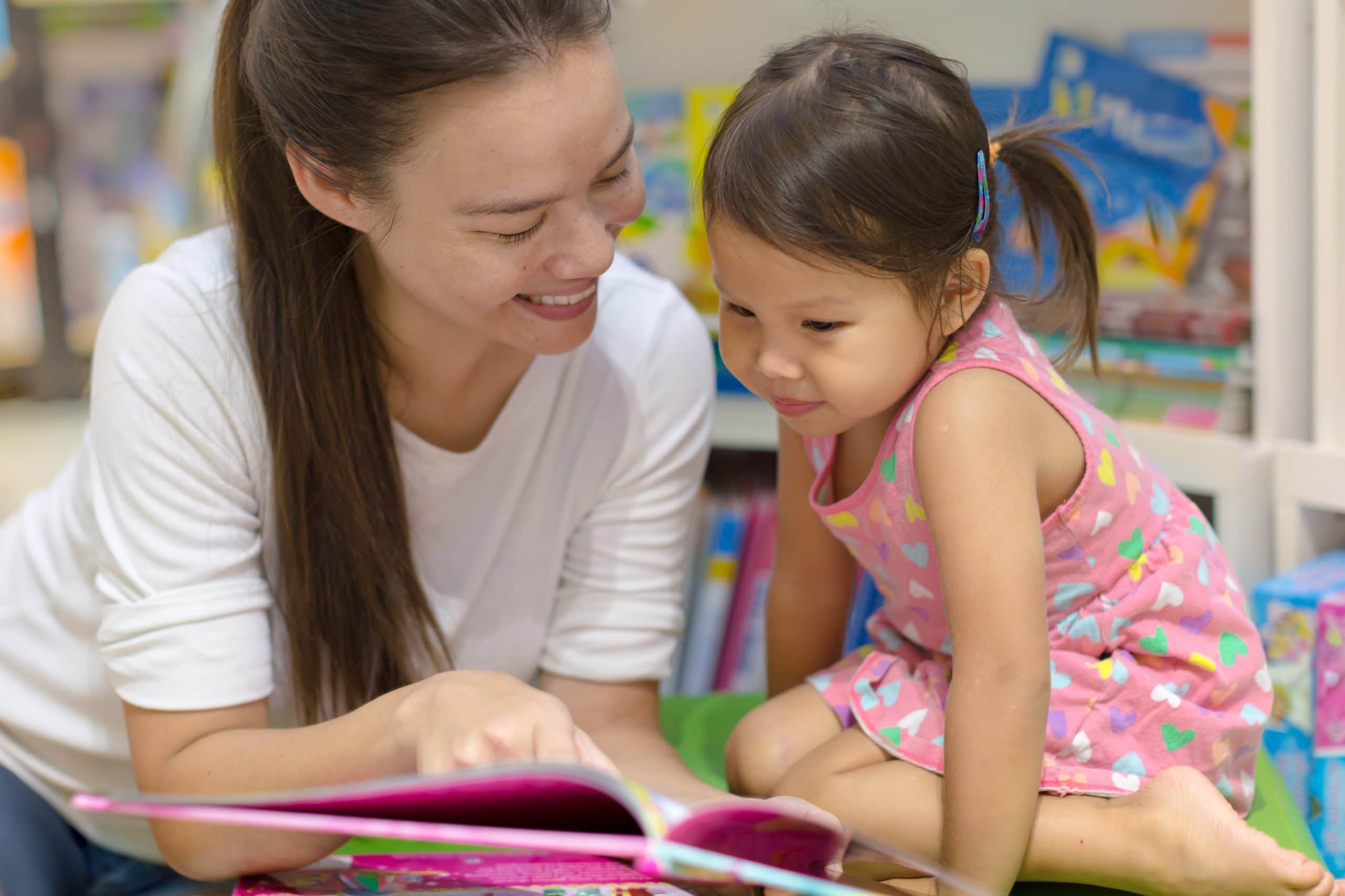 A teacher and student learn how to read together. The teacher is pointing at the book.