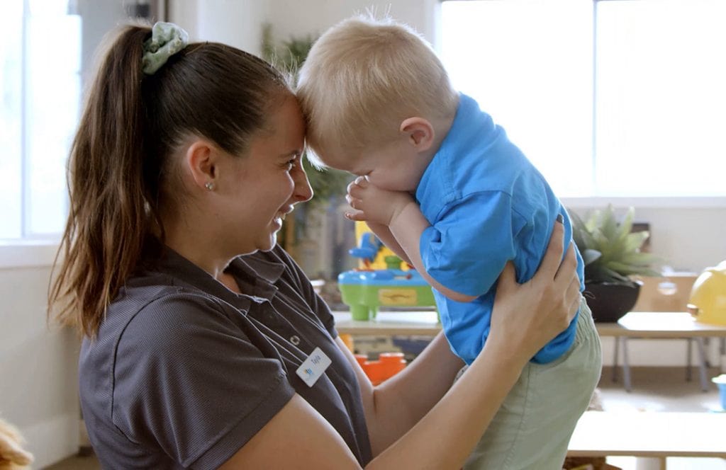 childcare worker playing with and lifting a child