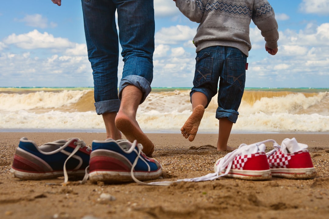 Two pairs of shoes taken off as father and son walk on the sand to the water at the beach