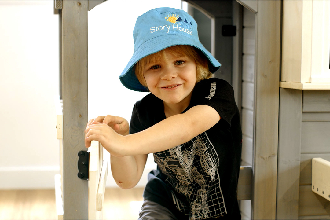 Child wearing a blue bucket hat with Story House logo