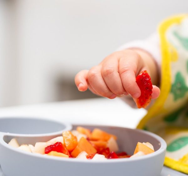 Close up of Baby Hand with a Piece of Fruits Sitting in Child's Chair Kid Eating Healthy Food