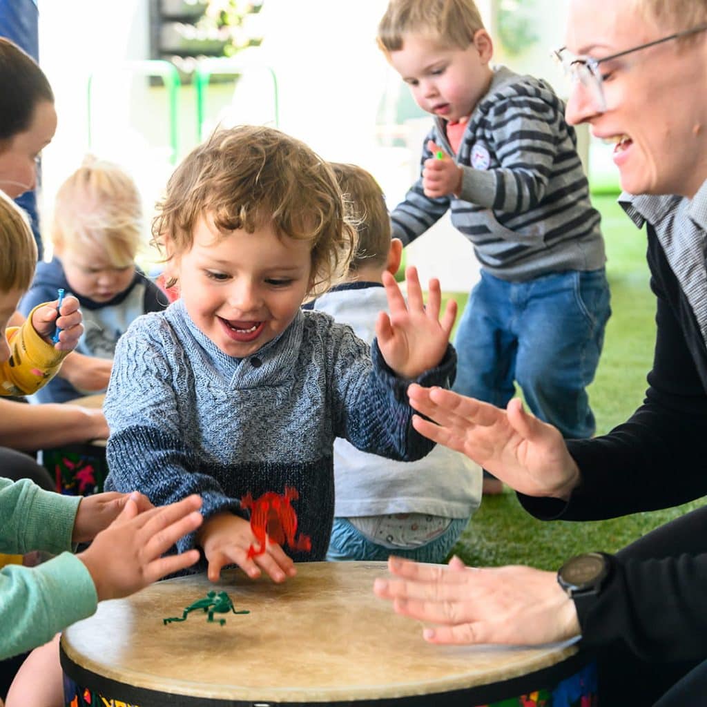 Two happy children playing the drums with an educator